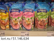 Supermarket shelves with various sauces of the Chumak brand. In the foreground, in soft packages, are Russian sauce with horseradish and Georgian sauce for meat. The packages are bright, with images of delicious dishes and greens, which emphasize the taste and culinary purpose of the product. At the bottom, the price tag indicates the cost of 0.89 euros for 200 grams. The photo illustrates the theme of a grocery store, Ukrainian sauces, the assortment in the supermarket and prices for products. Suitable for articles on nutrition, trade, marketing and consumer goods. (2015 год). Редакционное фото, фотограф Анна Кривицкая / Фотобанк Лори