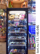 A display case with handmade chocolate in a store. Various candies and chocolate bars are neatly laid out on the shelves of a glass refrigerator – truffles, pralines, shaped chocolate, sweets with nuts, fruits and caramel. Some sets are packed in beautiful gift boxes with bows and ribbons. The inscription on the display case says: “Handmade chocolate”. The atmosphere of a cozy store with delicacies, surrounded by gift sets and packages. The image conveys an atmosphere of celebration, luxury and uniqueness, suitable for illustrations about sweets, gifts, handicrafts and gastronomy. (2015 год). Редакционное фото, фотограф Анна Кривицкая / Фотобанк Лори