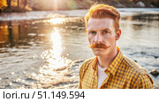 Red-Haired Man With Mustache Stands Near a River at Sunset. Generative AI. Стоковое AI-изображение, AI-художник Roman Zavorotny / Фотобанк Лори