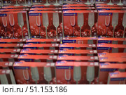 A shelf in a store with many boxes of Luminarc glasses. The boxes are decorated in bright red tones and feature elegant champagne flutes. Each box contains a set of three 175 ml glasses. The boxes are arranged in rows, creating a repeating pattern. The photo shows a selection of glassware in a supermarket or home improvement store, emphasizing the theme of shopping, table setting, and festive drinks. (2015 год). Редакционное фото, фотограф Анна Кривицкая / Фотобанк Лори