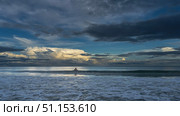 Dawn over the ocean. The waves roll towards the shore, spreading, foaming. The silhouette of a man in the water. The clouds in the blue sky are highlighted in gold. Early morning. Malaysia. Borneo. Стоковое фото, фотограф Вера Ивановна Кубарева / Фотобанк Лори