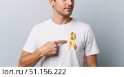 Сaucasian man stands with a yellow ribbon on a white t-shirt, pointing at it. Стоковое AI-изображение, AI-художник Екатерина Селезнева / Фотобанк Лори