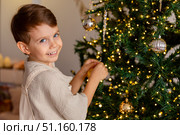 Side view of a cute happy little boy decorating a Christmas tree in the living room at home. Merry Christmas and happy New Year winter holidays. High-quality photo. Стоковое фото, фотограф Ирина Михайличенко / Фотобанк Лори