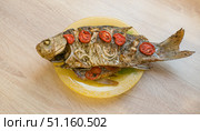 Baked large crucian fish with herbs, tomatoes and spices on a plate on the table. Стоковое фото, фотограф Екатерина Золина / Фотобанк Лори