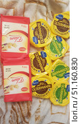 A photo of a selection of cheeses against a soft blanket. On the left are two large rectangular pieces of cheese in a red Milbona Edam package weighing 700g each. On the right are several round packages of Valio Oltermanni cheese, including the classic version in a yellow package and a lighter version with reduced fat content (17%) in a green package. The cheeses are neatly laid out, creating a composition that highlights the diversity of brands and types. The image can be used to illustrate food themes, healthy eating, dairy products or purchases from the store. (2019 год). Редакционное фото, фотограф Анна Кривицкая / Фотобанк Лори