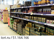 A supermarket department with shelves filled with a variety of coffee and tea. In the foreground, rows of packages of ground and bean coffee of different brands are visible, as well as boxes of tea bags. The assortment includes well-known brands, presented in packs, boxes and cans of different colors and sizes. Below are pallets with additional packages for replenishing the shelves. The background of the store is light, with wide aisles and additional products, which emphasizes the atmosphere of a modern sales area.The image is great for themes related to retail, supermarkets, coffee and tea selection, shopping, everyday shopping and food. (2015 год). Редакционное фото, фотограф Анна Кривицкая / Фотобанк Лори