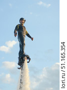 Athlete flyboarder smiles in close-up over the water. Flyboarding high above the water with a stunning sky backdrop during a sunny day. Стоковое фото, фотограф Владимир Разгуляев / Фотобанк Лори