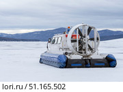 A hovercraft glides effortlessly over a snow-blanketed lake, surrounded by a serene winter landscape. The snow-covered surface reflects the cloudy sky, while distant mountains provide a picturesque. Стоковое фото, фотограф Владимир Разгуляев / Фотобанк Лори