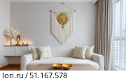 Sunlit living space featuring macrame wall art, spiritual decor elements, and plush seating, embodying relaxed bohemian design aesthetic. Стоковое AI-изображение, AI-художник Юрий Поздников / Фотобанк Лори