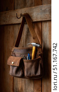 Weathered leather tool bag hanging on metal hook, vintage wooden backdrop. Hammer and tools partially visible, symbolizing skilled craftsmanship and practical heritage. Стоковое AI-изображение, AI-художник Юрий Поздников / Фотобанк Лори