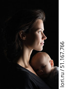 Soft light revealing intimate maternal bond, young mother cradling newborn against dark backdrop, gazing pensively with gentle protective embrace. Стоковое AI-изображение, AI-художник Юрий Поздников / Фотобанк Лори