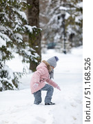 Side view of a little girl dressed in warm cozy clothes walking through a winter park or forest with knee-deep snow. Peaceful, chilly winter nature atmosphere. High quality photo. Стоковое фото, фотограф Ирина Михайличенко / Фотобанк Лори