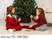 Two little girls friends play rock paper scissors hand game near Christmas tree at home. Children sit on a floor and playing together. Interesting entertaining activity for kids. High quality photo. Стоковое фото, фотограф Ирина Михайличенко / Фотобанк Лори