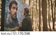 Thoughtful man stands in front of a painting depicting a man situated within a wooded environment. Стоковое AI-видео, аниматор Данила Большаков / Фотобанк Лори
