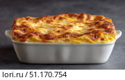 Close-up image of a freshly baked lasagna in a white ceramic baking dish. The top layer is golden brown with melted cheese, showcasing the delicious, rich, and hearty nature of this traditional Italian dish. The photo captures the warmth and appeal of homemade comfort food. Стоковое AI-изображение, AI-художник Ксения Чунаева / Фотобанк Лори
