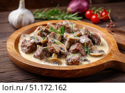 Meat and mushrooms. Dish of stir-fried beef fillet and mushrooms in a creamy thick sauce, served on an iron plate on a wooden board, close-up view. Gourmet food. Beef stroganoff large pieces. Stir Fry. Стоковое AI-изображение, AI-художник Марина Демидюк / Фотобанк Лори