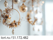 Delicate wreath of golden Christmas decorations hangs on the white wall. Magic and joy festive celebrations during the winter season. Elegant gold and silver Ornaments beautifully decorated setting. Стоковое AI-изображение, AI-художник Марина Демидюк / Фотобанк Лори