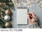 Woman's hand writing in empty notebook at the desk with Christmas decoration. Back to life, goal list. Plan, goals, checklist, idea concept. Top view, copy space. New Year. Blank White Paper Sheet. Стоковое AI-изображение, AI-художник Марина Демидюк / Фотобанк Лори