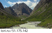 Mountain valley with rushing river, steep rocky slopes, green meadows, towering summits and visible trekking path ideal for mountaineering, backpacking and alpine exploration in Ala-Archa Alpine Camp. Стоковое видео, видеограф Андрей Ка / Фотобанк Лори