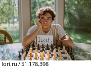 Юноша с табличкой 'I lost' за шахматной доской. Стоковое AI-изображение, AI-художник Дина Етова / Фотобанк Лори