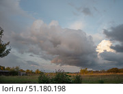 Large beautiful cumulus clouds in evening sunset sky above golden field and flowers in foreground, summer landscape. Стоковое фото, фотограф irisff / Фотобанк Лори