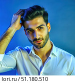 Young Turkish Man With Stubble Runs Hand Through Hair in Blue Lit Studio. Generative AI. Стоковое AI-изображение, AI-художник Roman Zavorotny / Фотобанк Лори