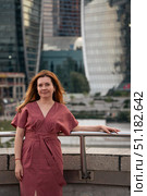 Woman in a burgundy dress poses against the backdrop of the modern skyscrapers of Moscow City. Стоковое фото, фотограф Софья Соломонова / Фотобанк Лори