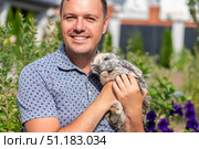 Portrait of caring smiling man holding cute fluffy lop-eared rabbit in backyard of garden outdoors. Стоковое фото, фотограф Данила Большаков / Фотобанк Лори