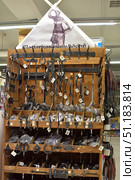 A stand with hand-forged metal products in a store or at a fair. Various forged elements are hung and laid out on wooden shelves and hooks: hinges, hooks, handles, locks, rings, decorative holders, elements for doors and gates. At the top of the stand there is an advertising poster with an image of a blacksmith and the inscription in Finnish "Mestarisepät aito käsityö", which translates as "Masters of blacksmithing, real craft". All products are made in a traditional style, emphasizing the rough texture of the metal, and are intended for both practical use and for decorative interior or exterior design. (2015 год). Редакционное фото, фотограф Анна Кривицкая / Фотобанк Лори