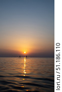 Paddle boarders gliding across calm waters, silhouetted against vibrant sunset sky, sharing serene maritime moment. Стоковое фото, фотограф Данил Руденко / Фотобанк Лори