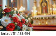 Beautiful Christmas floral arrangement with red, white, and gold flowers in a church setting, symbolizing festive holiday spirit and religious celebration. The warm candlelight and blurred altar in the background create a sacred, peaceful ambiance. Suitable for illustrating Orthodox Christmas in Russia and Eastern Europe. Стоковое AI-видео, аниматор Ксения Чунаева / Фотобанк Лори