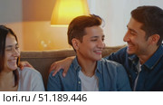Three friends enjoy a joyful evening at home, sharing smiles and laughter while sitting comfortably on a couch under warm lighting. Стоковое AI-видео, аниматор Данила Большаков / Фотобанк Лори