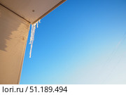 Long icicles dangle from the edge of a roof, capturing sunlight and glistening against a clear blue sky. This winter scene evokes a sense of tranquility and the beauty of cold weather. Стоковое фото, фотограф Юлия Петровская / Фотобанк Лори