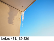 Long icicles dangle from the edge of a roof, capturing sunlight and glistening against a clear blue sky. This winter scene evokes a sense of tranquility and the beauty of cold weather. Стоковое фото, фотограф Юлия Петровская / Фотобанк Лори