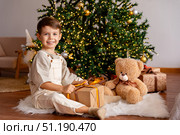 Happy little boy opens a gift box while sitting on a fur carpet near Christmas tree. Child is happy with a New Year gift. The concept of Christmas and New Year holidays. High quality photo. Стоковое фото, фотограф Ирина Михайличенко / Фотобанк Лори