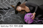 Beautiful witch girl in a witch's cap holds a lilac lantern in her hands against the background of a white web on Halloween. Стоковое видео, видеограф Катерина Белякина / Фотобанк Лори