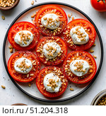 Холодная закуска из кружочков помидоров со сметаной и кедровыми орехами лежит на белой тарелке на белом столе. Вид сверху. Стоковое AI-изображение, AI-художник Мария Ульянова / Фотобанк Лори