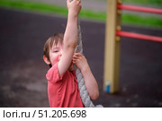 A child swinging on a rope at a playground. Young boy playing and having fun on adventure equipment. Outdoor activity and childhood concept. A child aged 3 years. Стоковое фото, фотограф Андрей Журавлев / Фотобанк Лори
