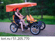 Woman riding a four-wheeled pedal bike on a paved path in a green park. Outdoor recreation and active lifestyle concept for summer. Стоковое фото, фотограф Андрей Журавлев / Фотобанк Лори