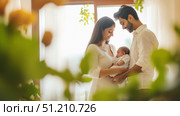 Young indian couple lovingly cares for baby in warm home setting. Стоковое AI-изображение, AI-художник Анастасия Золотницкая / Фотобанк Лори