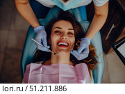 Улыбающаяся девушка проходит осмотр у стоматолога, который держит инструменты у ее рта, вид сверху. Стоковое AI-изображение, AI-художник Кирилл Сиротюк / Фотобанк Лори