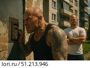 Intense Confrontation: Two Men in a Gritty Urban Setting, Displaying Tension with One Attentively Listening at the Door Intercom. Стоковое AI-изображение, AI-художник Башкирова Анна / Фотобанк Лори