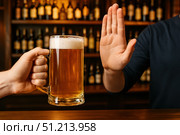 A Hand Offering a Glass of Beer is Met with a Refusal Gesture from Another Hand Against a Backdrop of Bottles in a Bar Setting. Стоковое AI-изображение, AI-художник Башкирова Анна / Фотобанк Лори