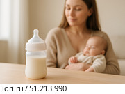 A Tranquil Moment: A Caring Mother Holds Her Sleeping Baby with a Bottle of Milk on the Table, Emphasizing Nurturing and Bonding in Parenting. Стоковое AI-изображение, AI-художник Башкирова Анна / Фотобанк Лори