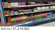 A refrigerated shelf in a supermarket with a wide range of drinks and dairy products. Brightly colored packages of juices, smoothies, milkshakes, yogurts and herbal drinks are arranged in neat rows on the shelves. You can see packages of different colors: green, red, pink, white and black, which creates a colorful palette and emphasizes the diversity of the assortment. On the lower shelves are packages of juices and nectars in cardboard packaging, above - bottles of protein drinks and smoothies. On the right, you can see yogurts in plastic cups and cardboard packaging. Below the shelves are attached price tags with information about the cost of goods. The atmosphere of the photo conveys the everyday look of a grocery store, the orderliness and availability of goods. (2019 год). Редакционное фото, фотограф Анна Кривицкая / Фотобанк Лори