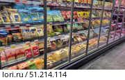 A supermarket display case with a large assortment of sliced ​​and packaged cheeses. The shelves feature various brands and types of cheese: Russian, cream, Gouda, Cheddar, Mozzarella, Edam and others. The packages are brightly colored - blue, green, red, yellow, which makes the display attractive to customers. All products are neatly laid out in a refrigerated section with transparent doors, which emphasizes freshness and proper storage conditions. The price tags indicate promotions and discounts, which creates the feeling of a real store. Редакционное фото, фотограф Анна Кривицкая / Фотобанк Лори