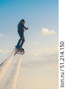 A person skillfully operates a flyboard, soaring high above a serene body of water. The golden light of sunset enhances the scene, creating a stunning backdrop. Стоковое фото, фотограф Владимир Разгуляев / Фотобанк Лори