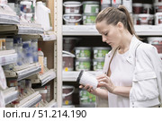 Woman in white clothes holds a jar of paint in a store and examines its paint composition. Buying paint color . Woman examines paint jar while shopping for color options and checking toxicity in a home improvement store. Стоковое фото, фотограф Владимир Разгуляев / Фотобанк Лори