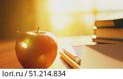 A vibrant red apple rests on a wooden table next to books and pencils, illuminated by warm afternoon sunlight streaming through the window. Стоковое AI-видео, аниматор Данила Большаков / Фотобанк Лори
