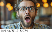 A man with curly hair and glasses shows a surprised expression while enjoying a relaxed afternoon in a café filled with warm lighting. Стоковое AI-видео, аниматор Данила Большаков / Фотобанк Лори